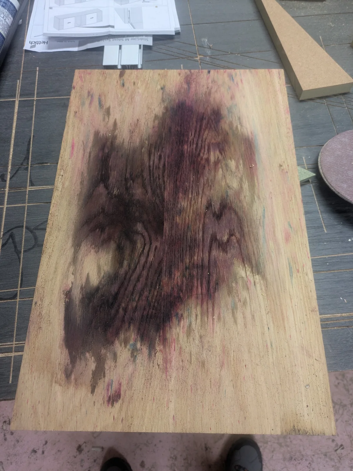 Dark dye stains spread across a bare wooden sample in the workshop