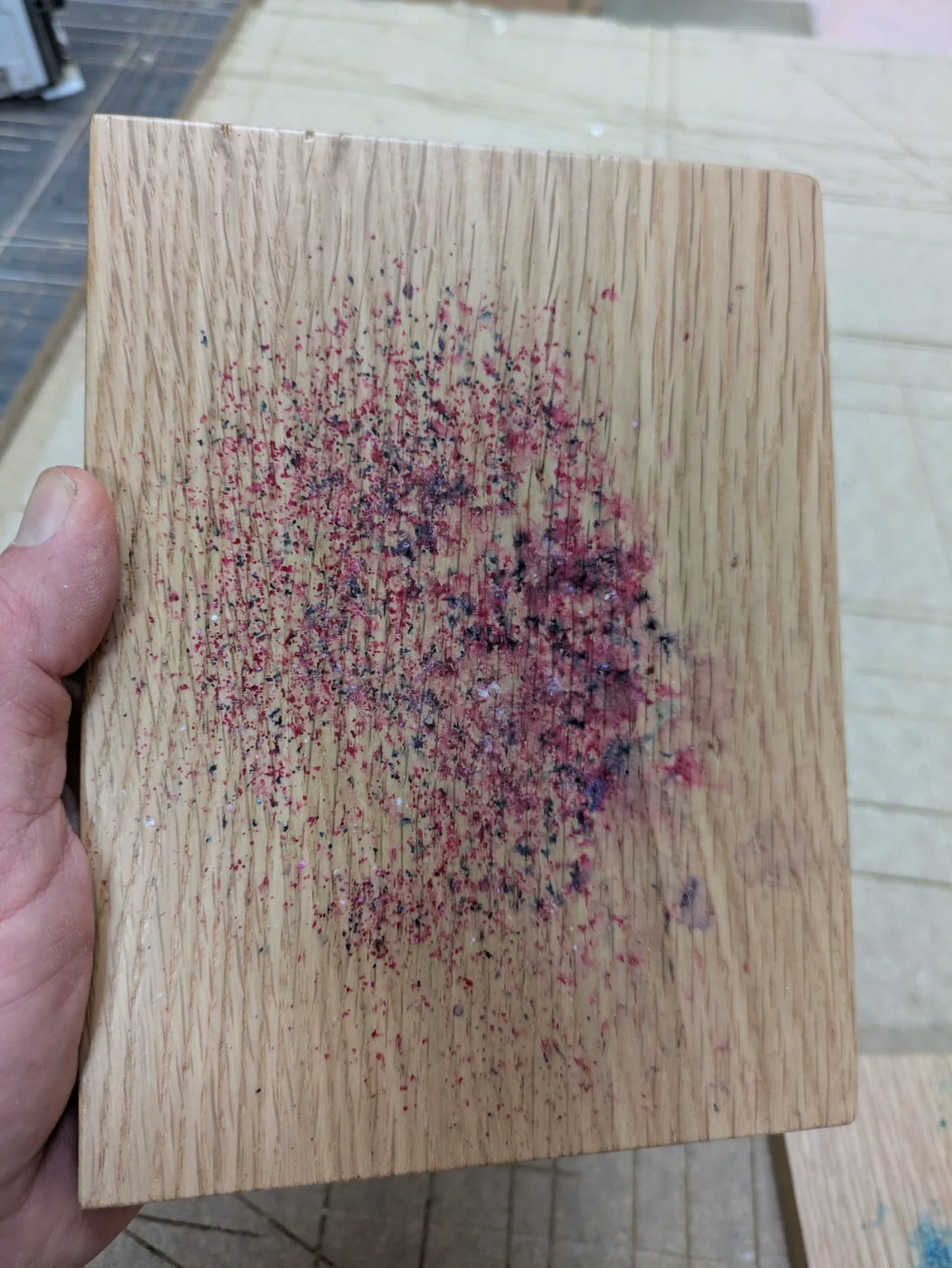 Close view of pink and dark dye crystals on an oak sample