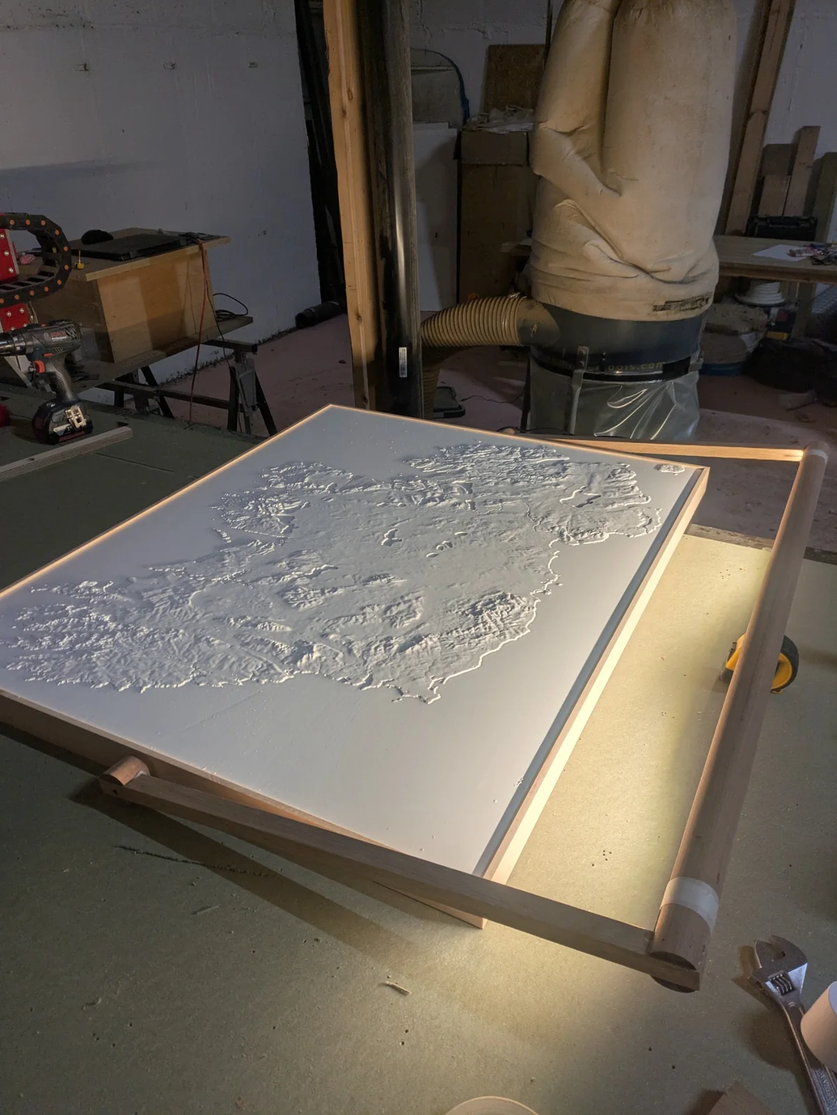 The framed white terrain model with its light arm being fitted on the bench